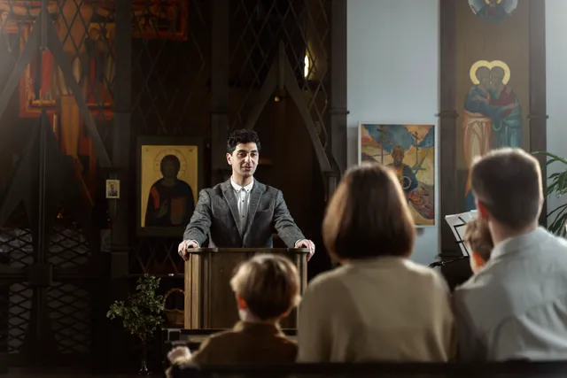 A person preaching from a lectern to a seated congregation