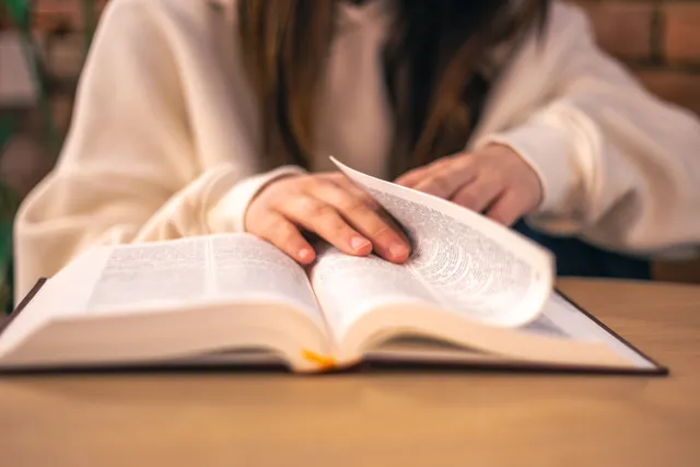 Hands turning the pages of an open bible on a table