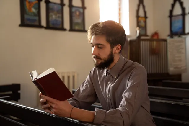 A person sitting in a pew reading, lit by a window