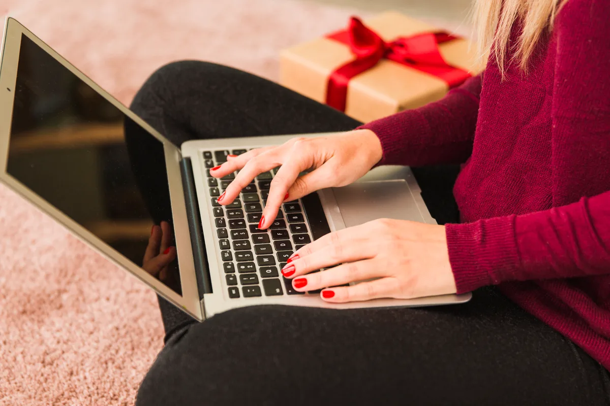 Hands typing on a laptop beside a wrapped gift box
