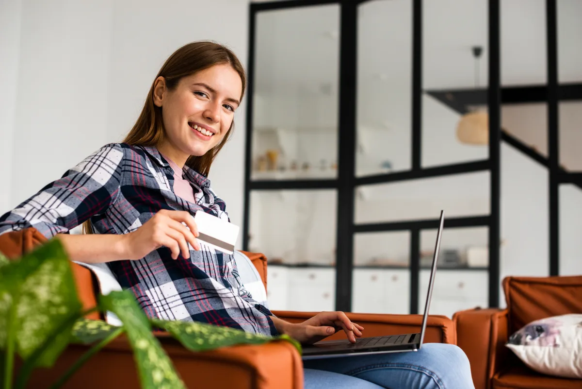 Someone watching on a laptop from a sofa, holding a payment card