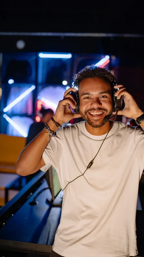 A host smiling at camera while pulling on a headset in a neon-lit gaming studio