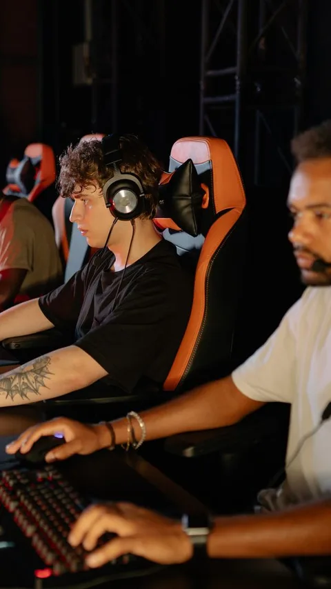 Players in headsets at a row of competition PCs, one leaning in behind another