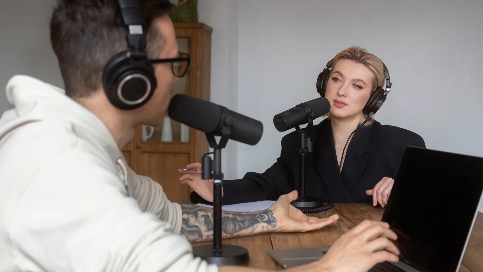 Wide podcast shot: two hosts on either side of a table with microphones between them